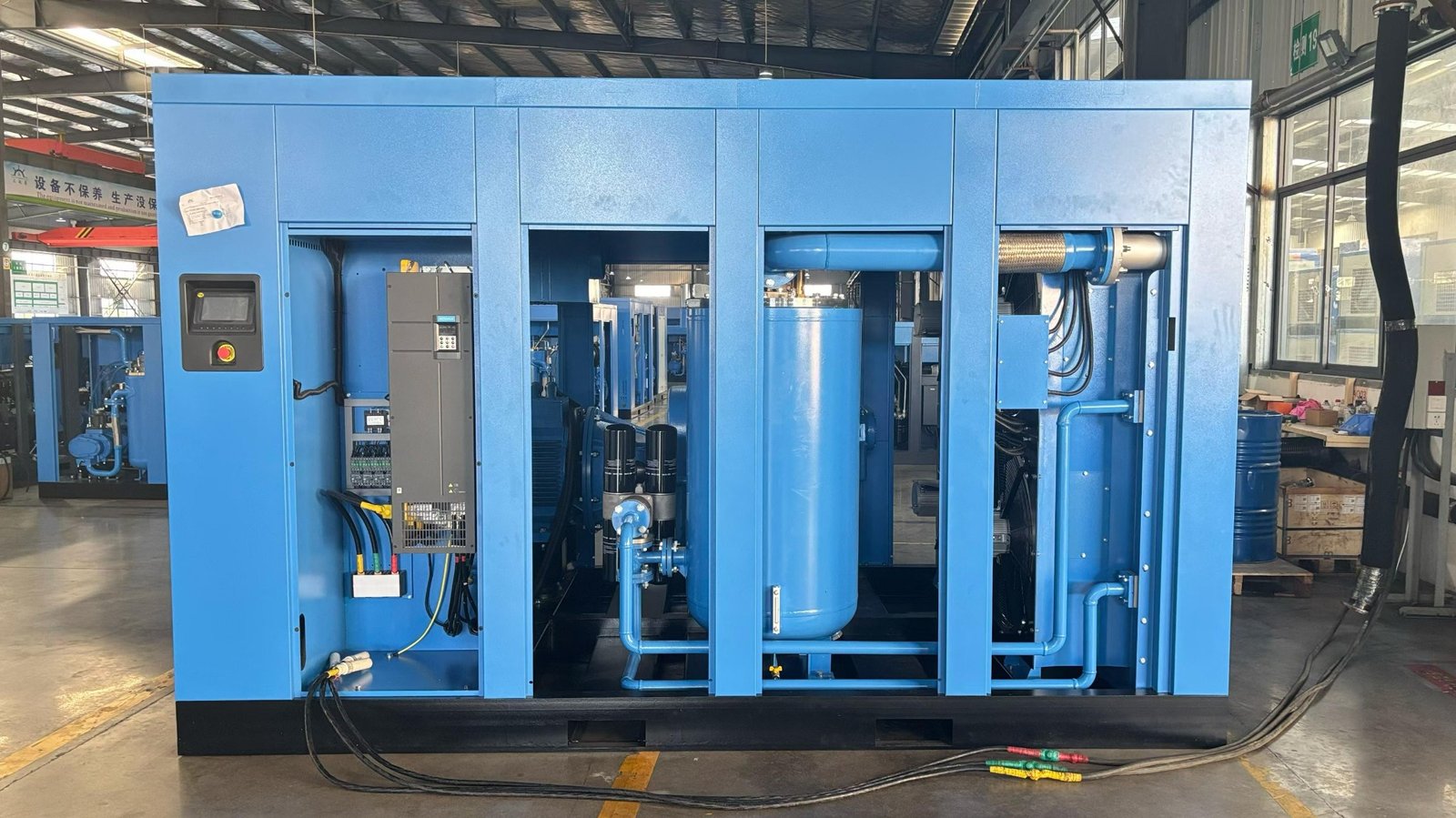 Large screw air compressor with side panels open and test cables connected on the workshop floor