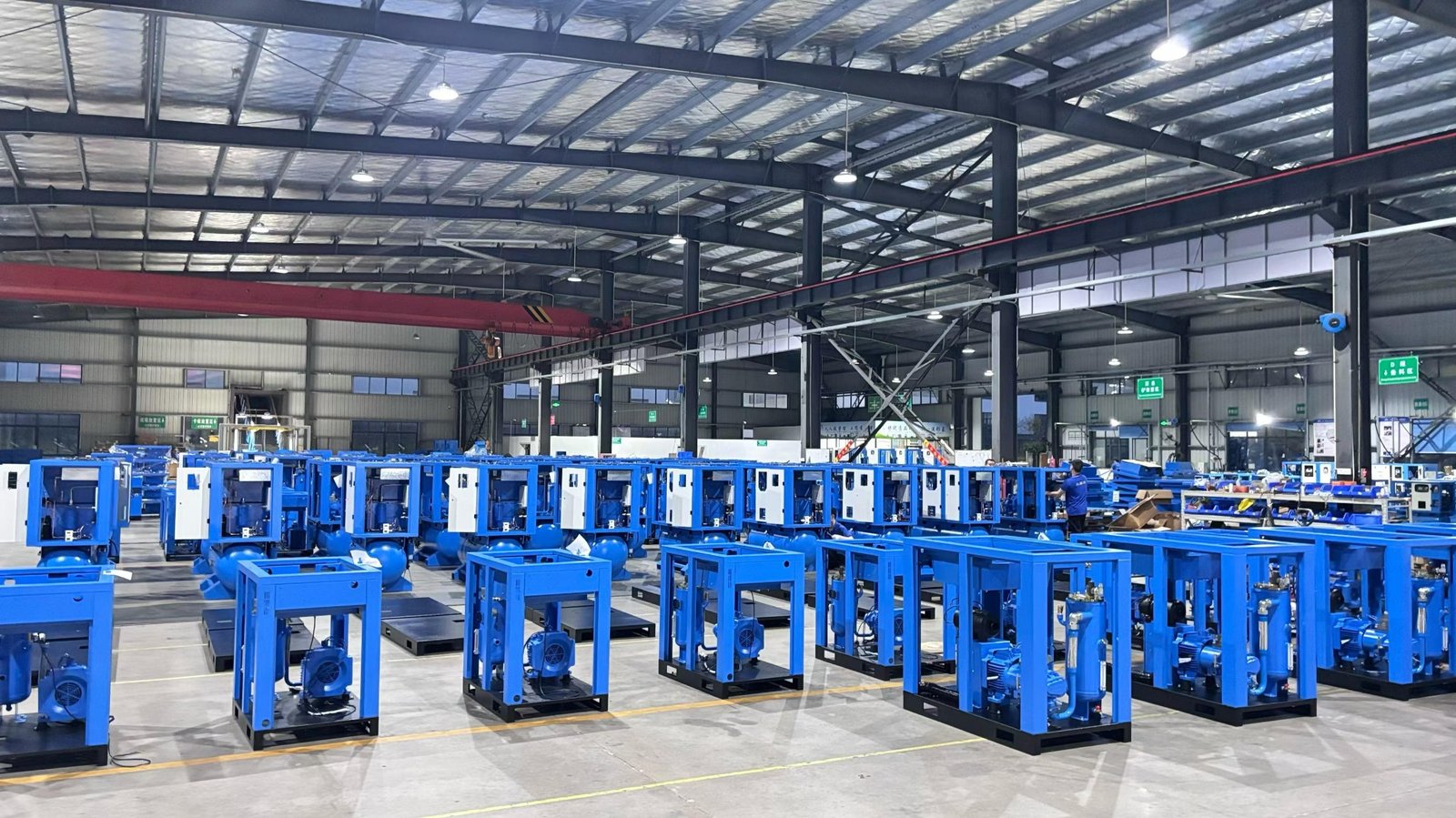 Rows of single-stage screw air compressor frames and integrated packages being assembled in the workshop